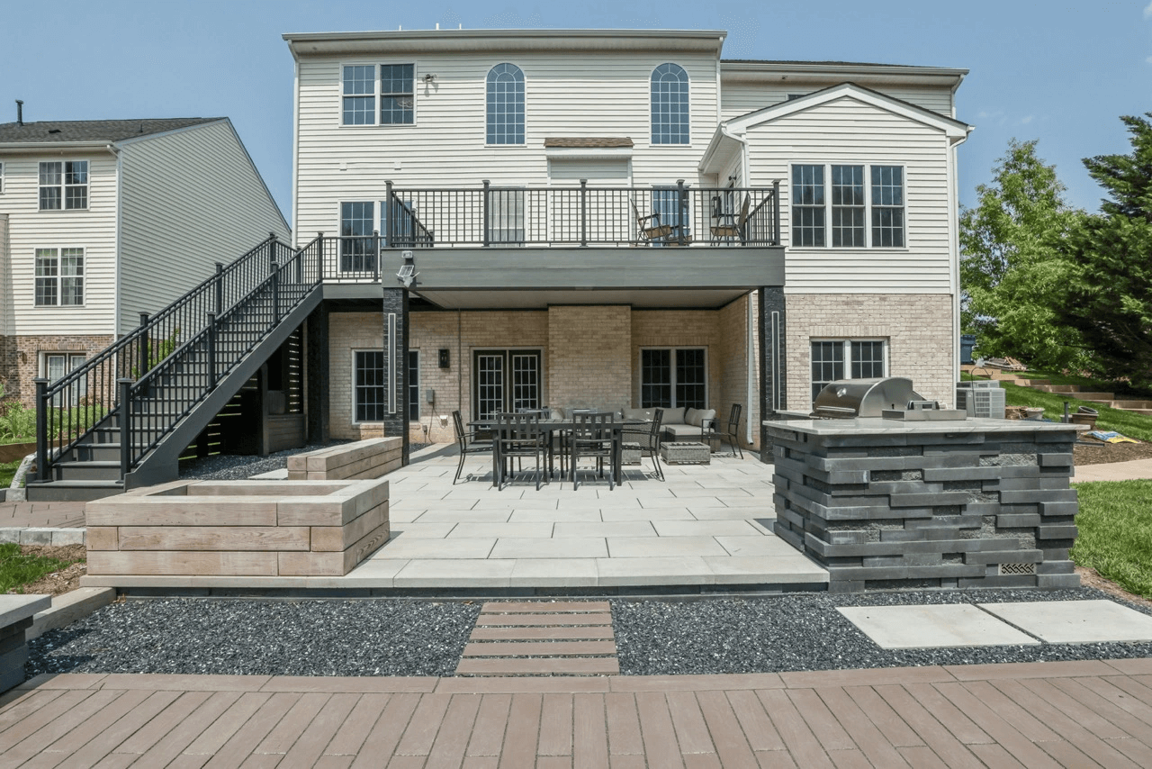2 story building with a deck on the second level. Stairs leading down to a custom patio with an outdoor kitchen