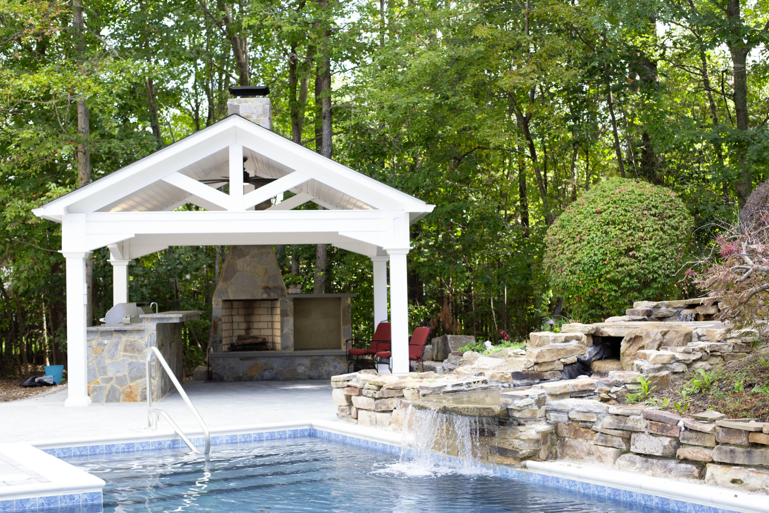 White pavilion over outdoor custom stone mosaic outdoor kitchen with pool in the front.
